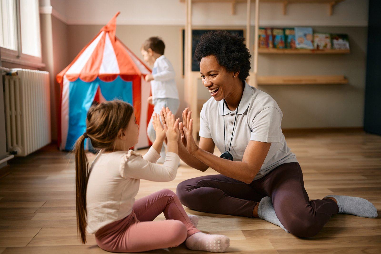 Happy African American teacher and little girl playing clapping game in the kindergarten.